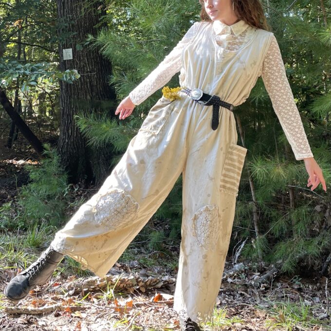 A woman in a tan jumpsuit standing in the woods.
