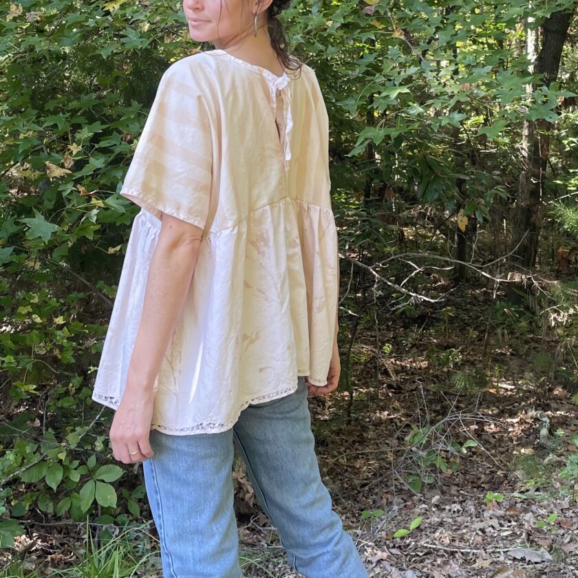 A woman is standing in the woods wearing jeans and a blouse.