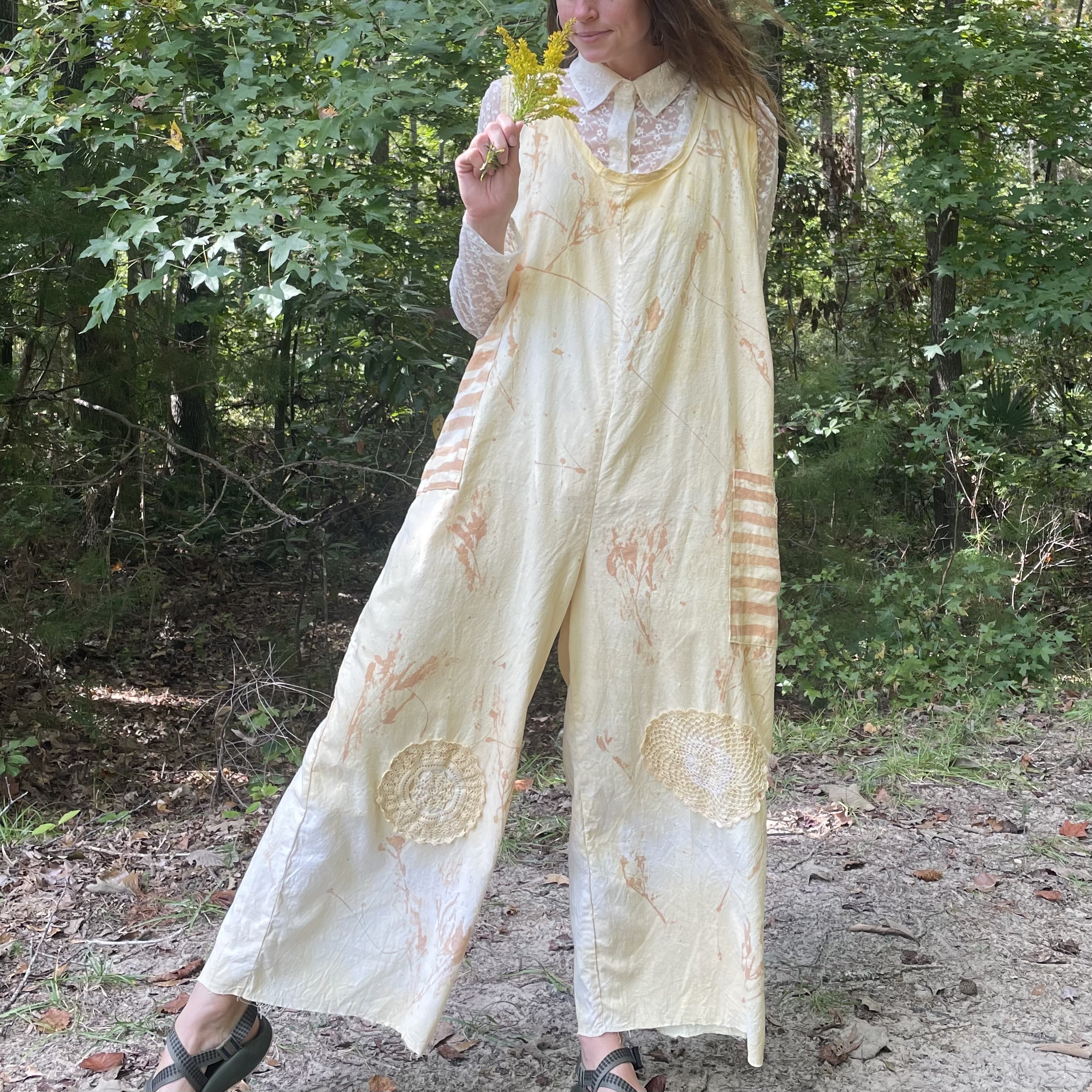A woman is standing in the woods wearing a yellow jumpsuit.