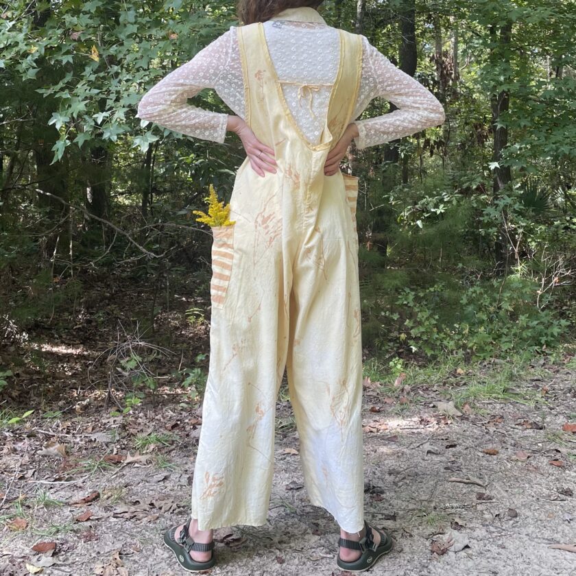 A woman in yellow overalls standing in the woods.