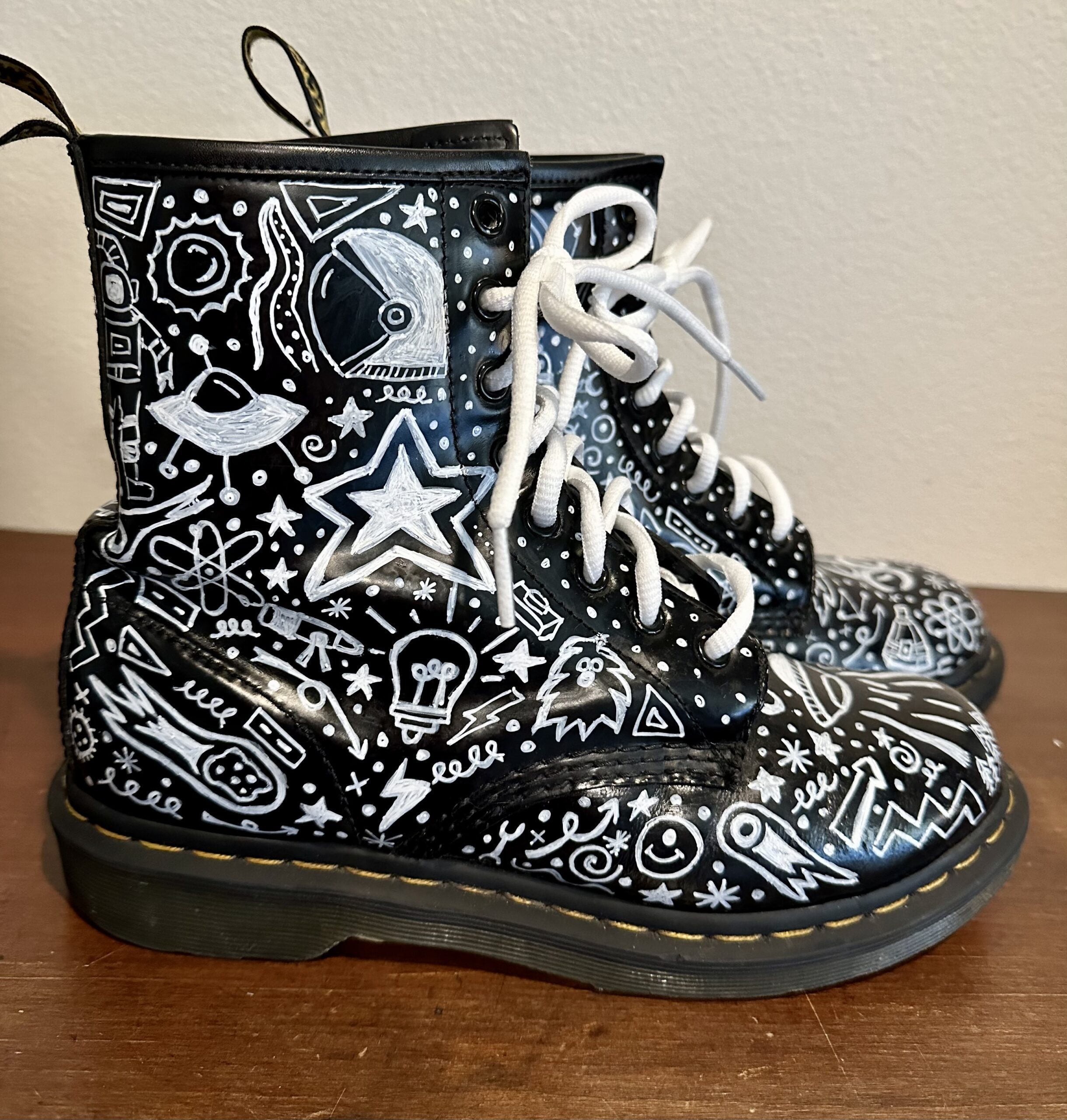 A pair of black and white dr martens boots with doodles on them.