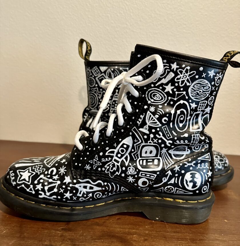 A pair of black and white dr martens boots with doodles on them.