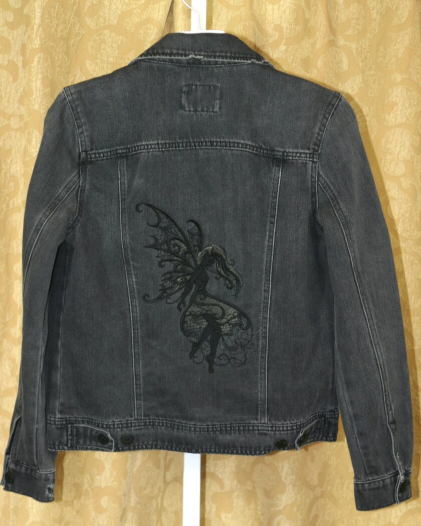 A black denim jacket with an image of a fairy on it.