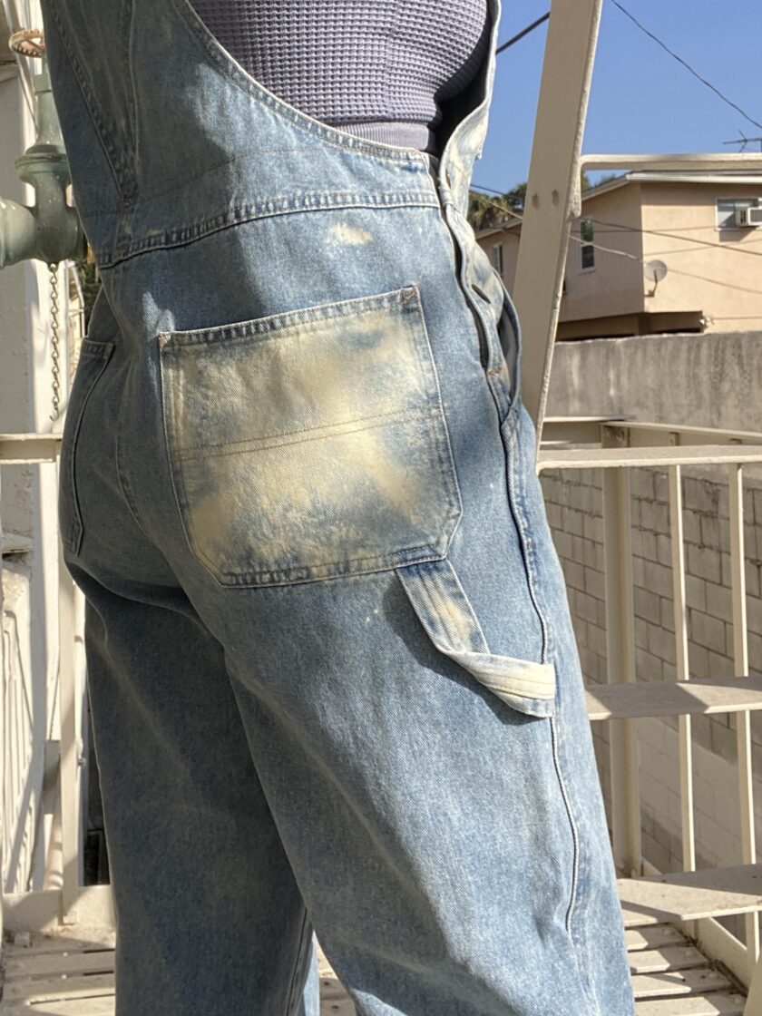 A woman is standing on a balcony wearing overalls.
