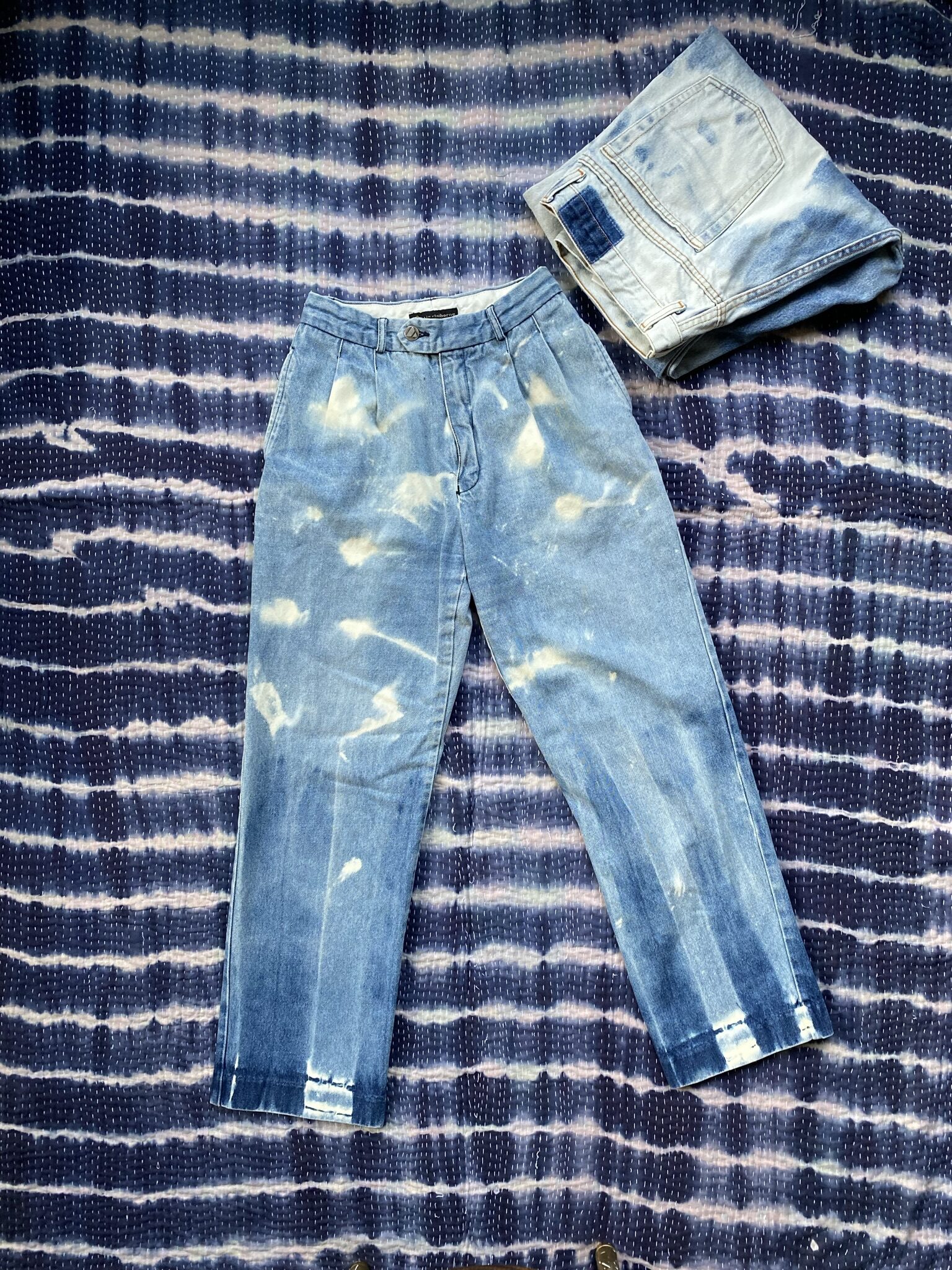 A pair of bleached blue jeans on a bed indigo tie dyed blanket.