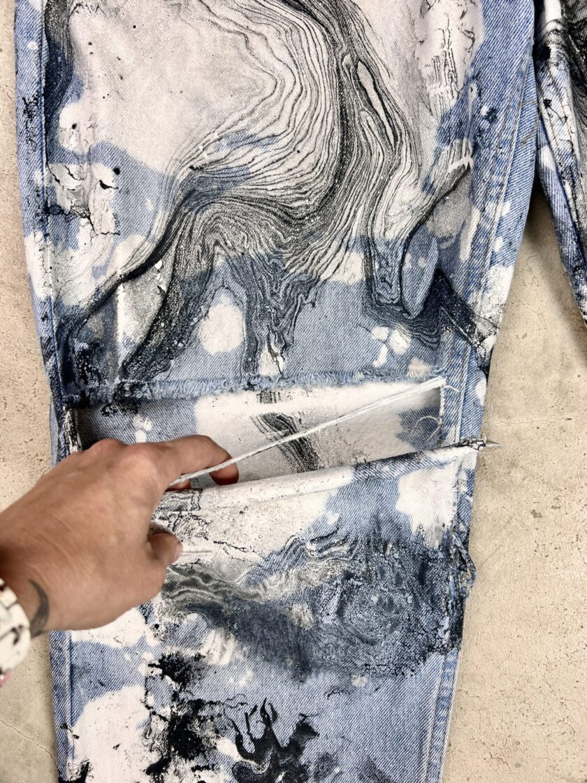 A person is holding a pair of jeans with paint on them.