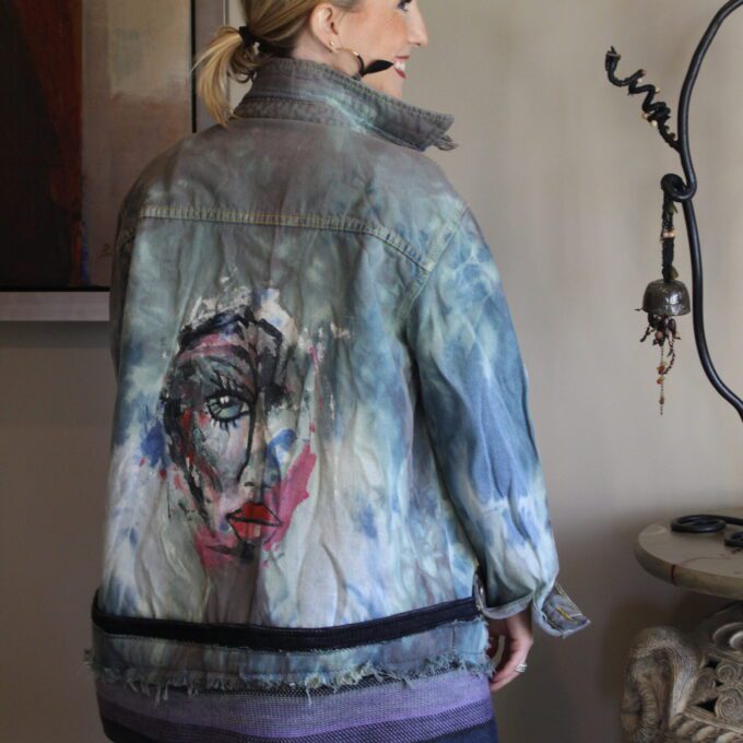A woman wearing a denim jacket with a painting on it.