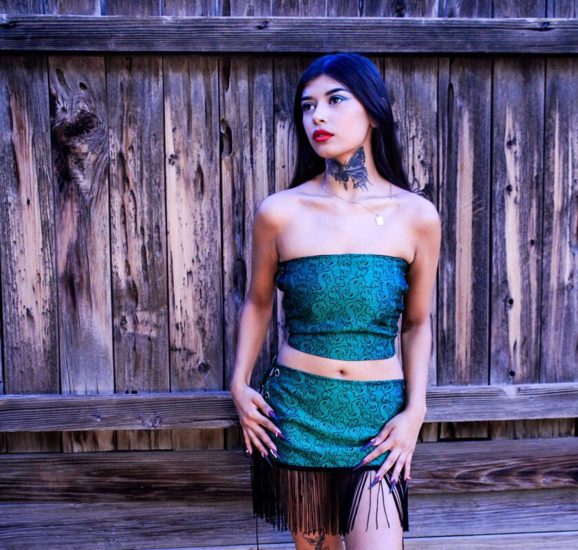 A woman in a green skirt posing in front of a wooden fence.