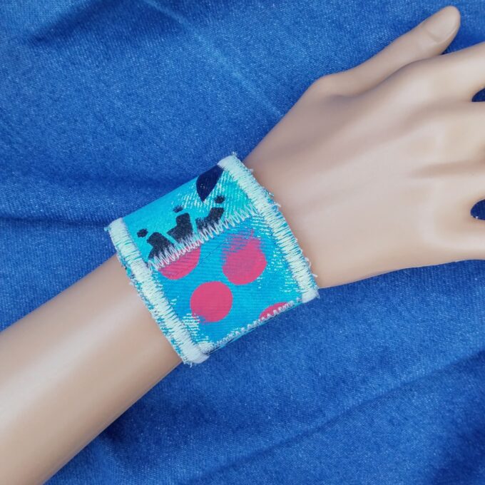 A upcycled denim cuff bracelet with blue gears and red polka dots.