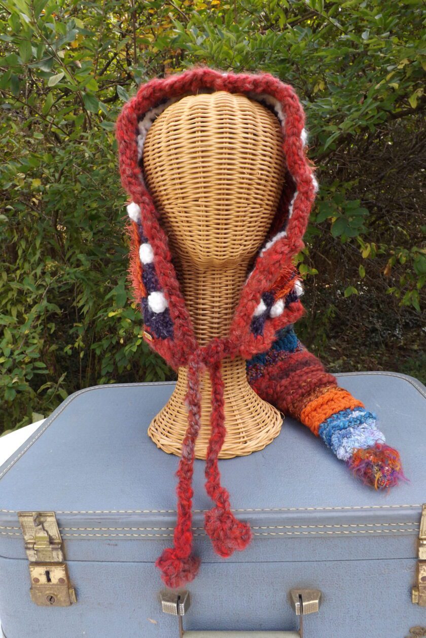 A crocheted hooded hat on top of a suitcase.