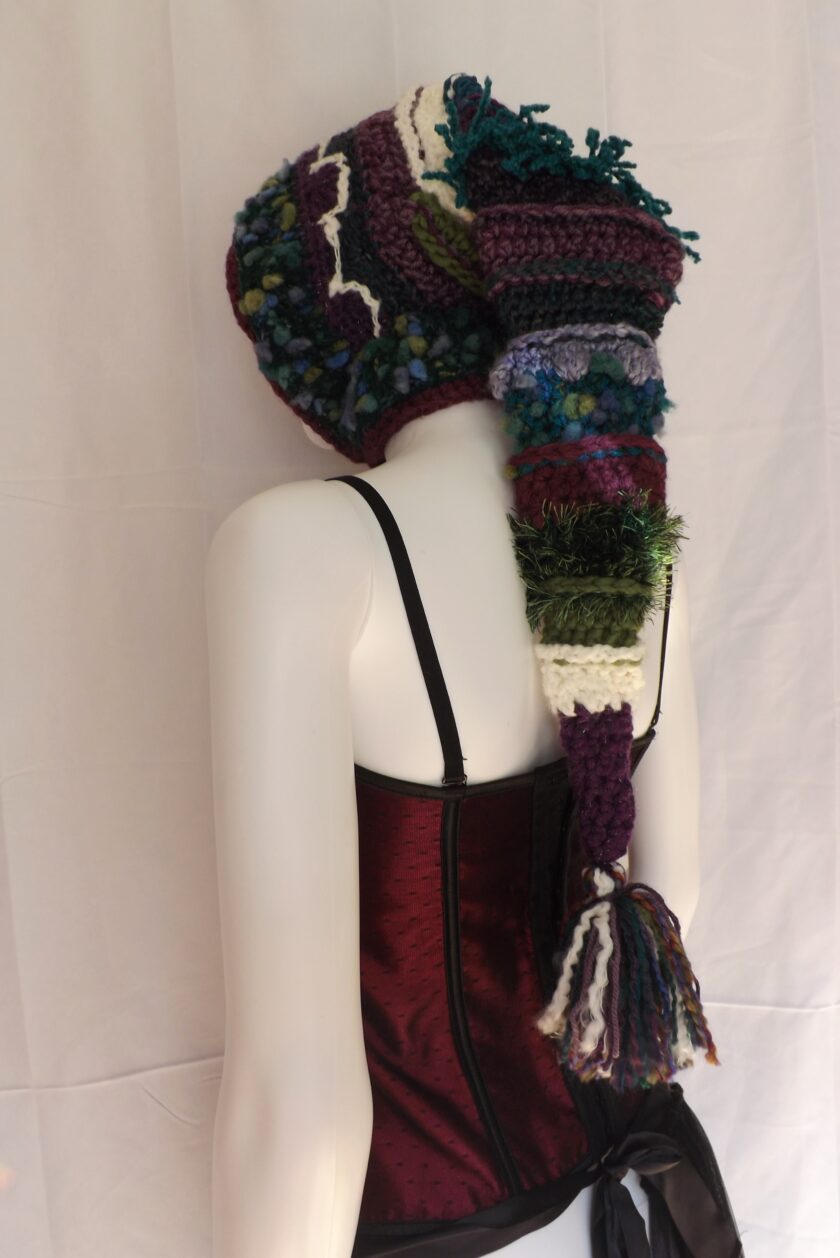A long crochet elf hood in shades of purple and teal.