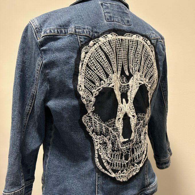 The back of a denim jacket with a skull embroidered on it.