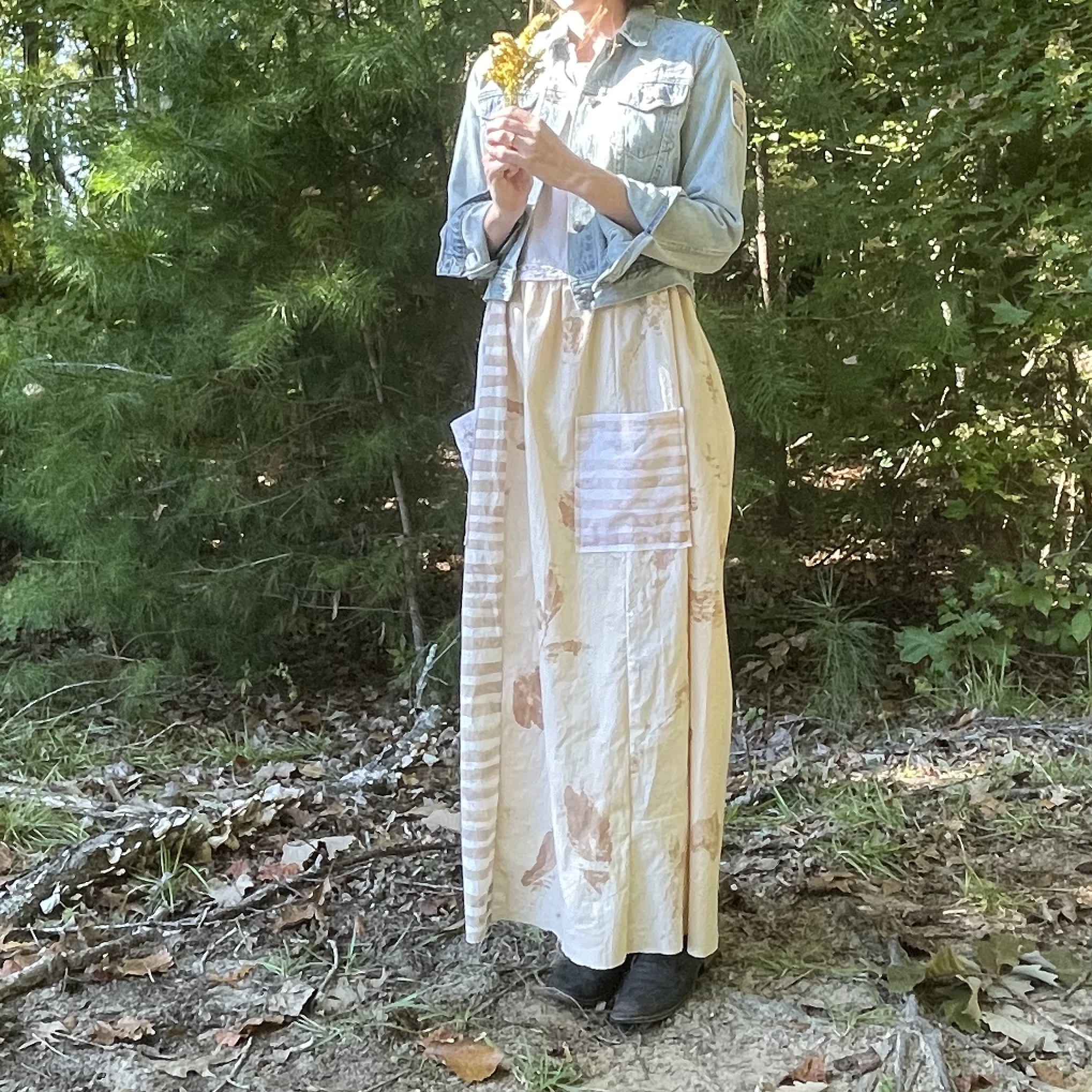 A woman is standing in the woods wearing a long skirt.