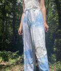 A woman is standing in the woods wearing indigo tie dyed pants.