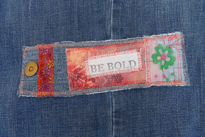 A denim and floral cuff bracelet with Be Bold printed on it