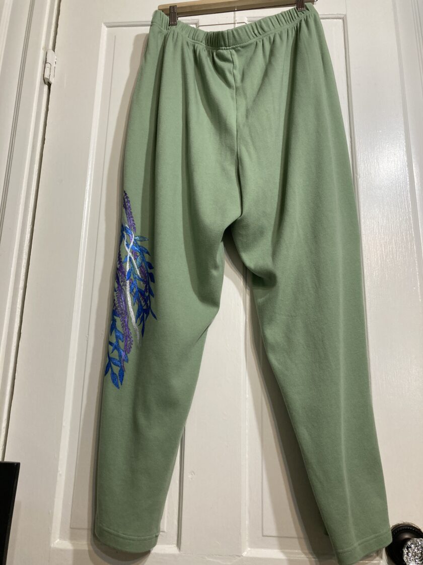 A pair of hand-painted green sweatpants hanging on a door.