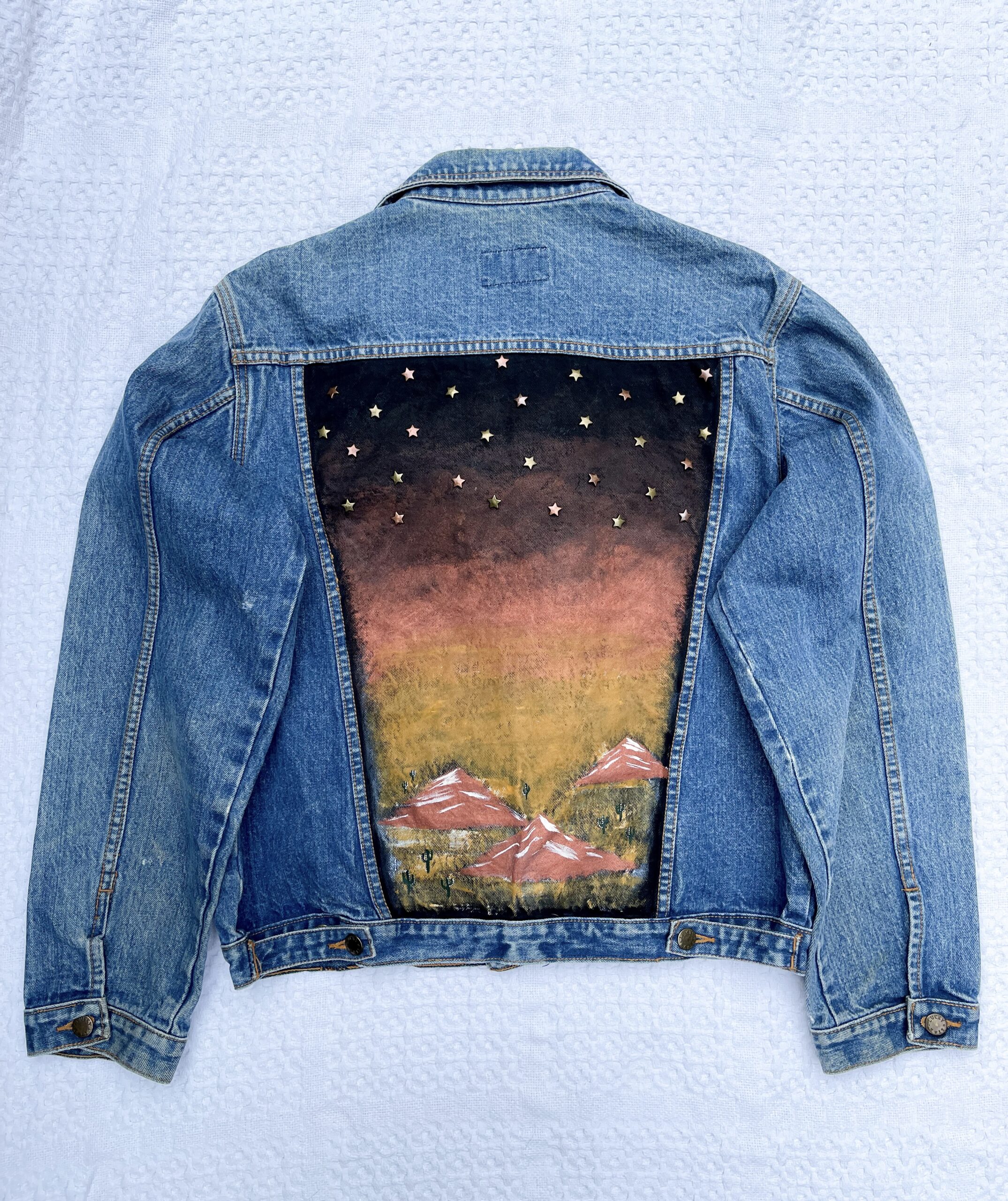 A denim jacket with a painting on the back.
