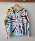 A tie dye hoodie hanging on a wooden hanger.