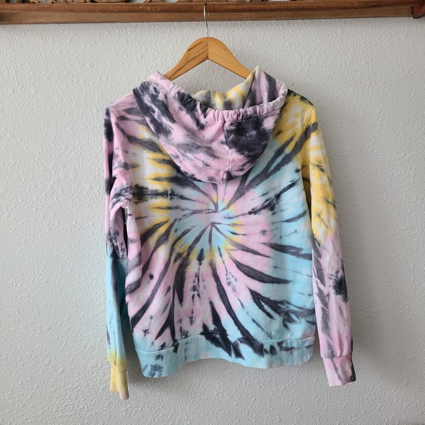 A tie dye hoodie hanging on a wooden hanger.