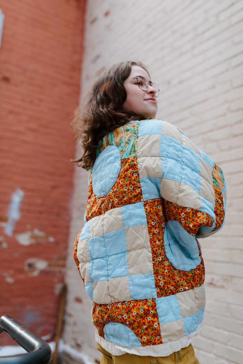 A woman wearing a quilted jacket in front of a brick wall.