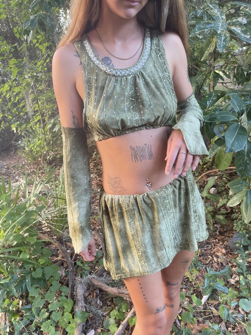 A woman wearing a green velvet top and shorts in the woods.