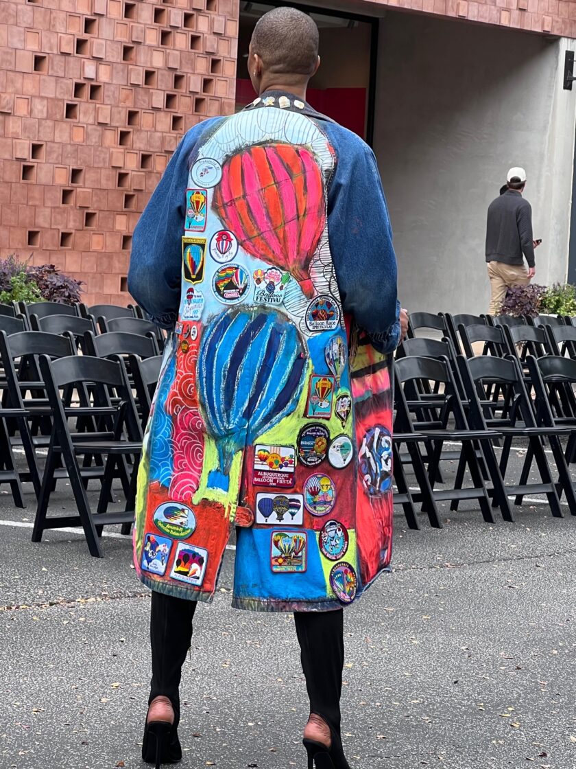 A woman wearing a colorful denim jacket walking down the street.
