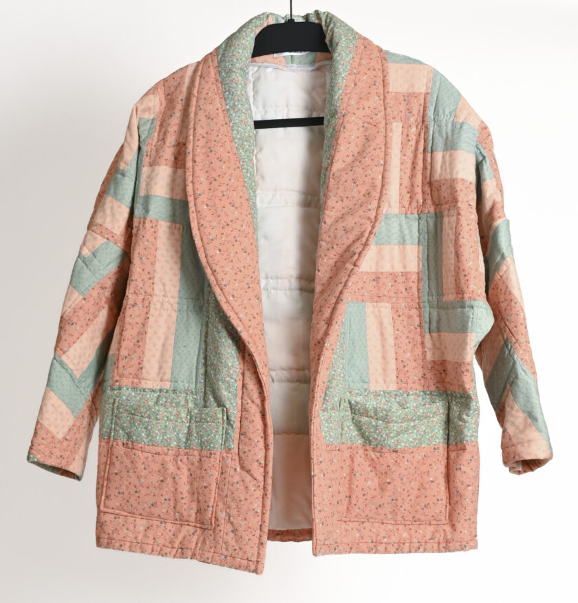 A pink and green quilted jacket hanging on a hanger.