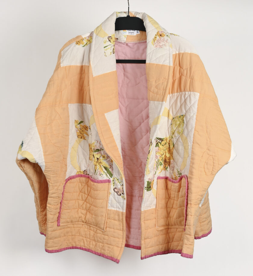 An orange and pink quilted jacket hanging on a hanger.