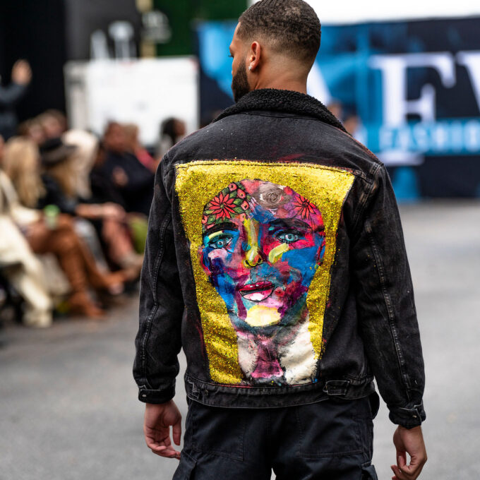 A man walking down the street wearing a jacket with a painting on it.