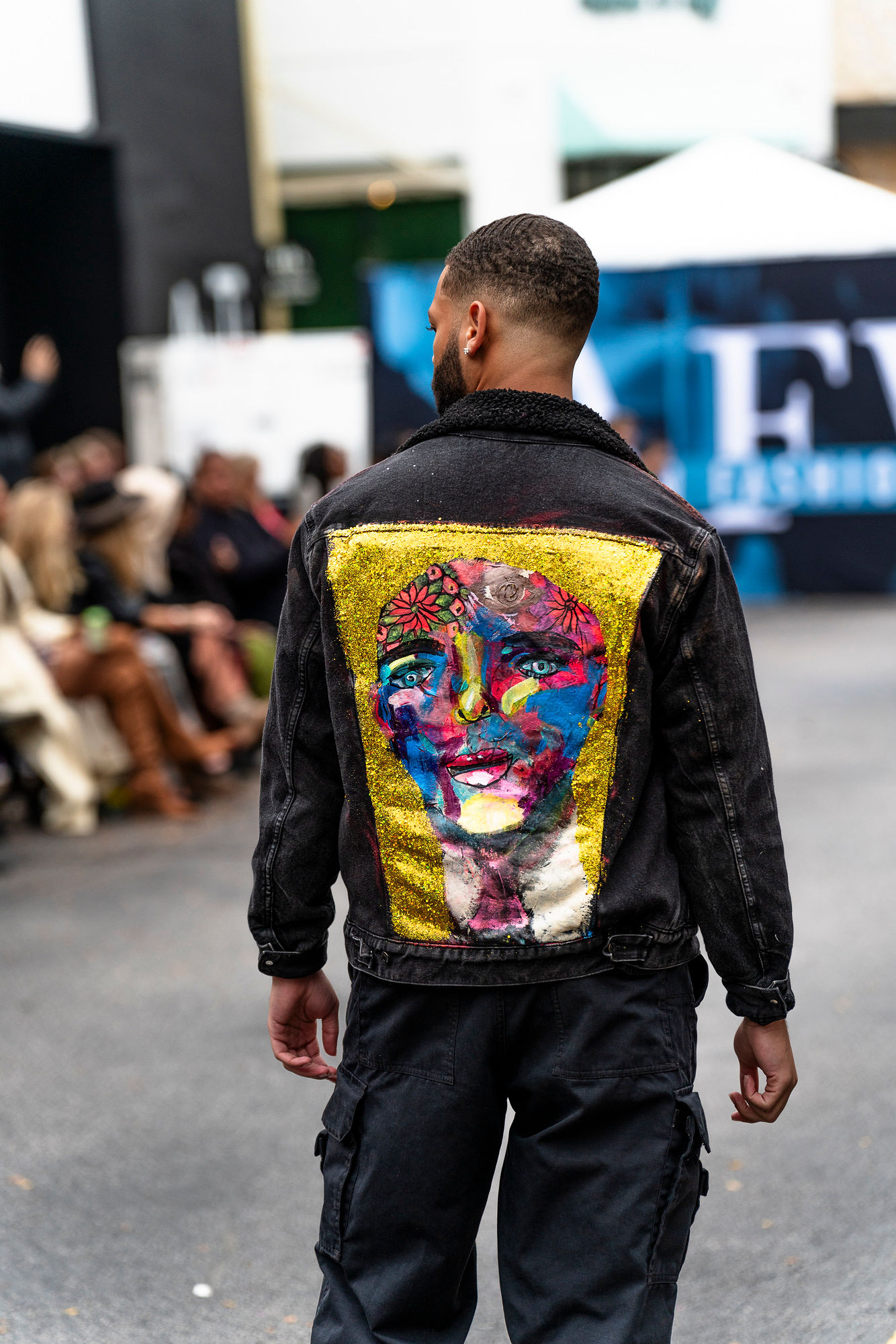 A man walking down the street wearing a jacket with a painting on it.