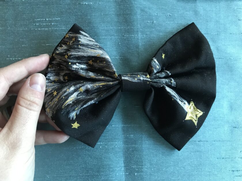 A hand holding a large hand-painted black bow with stars