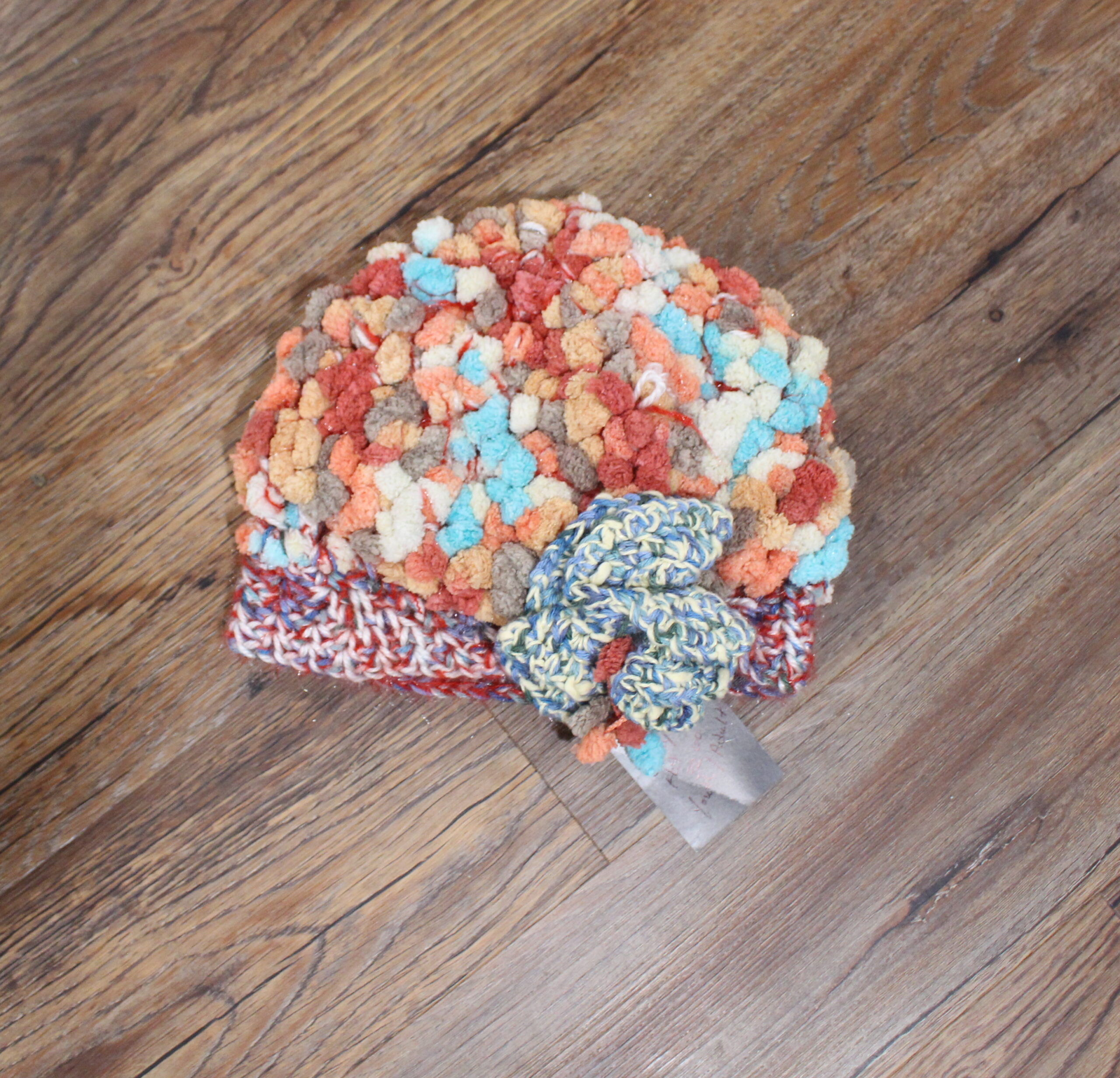 A colorful pom pom hat on a wooden floor.