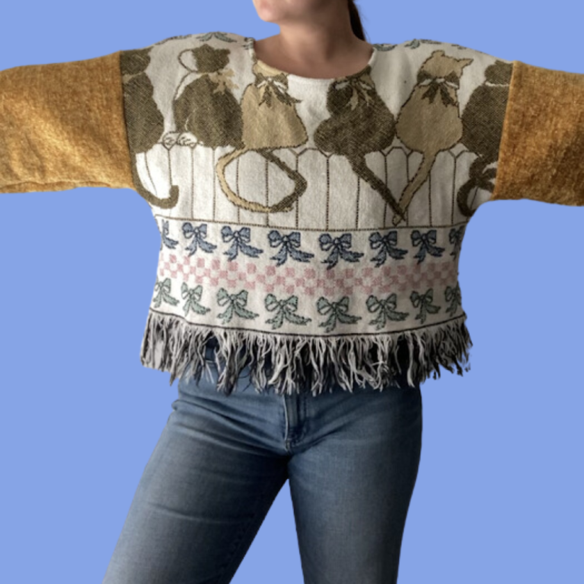 A woman wearing a sweater with fringes and a cat on it.