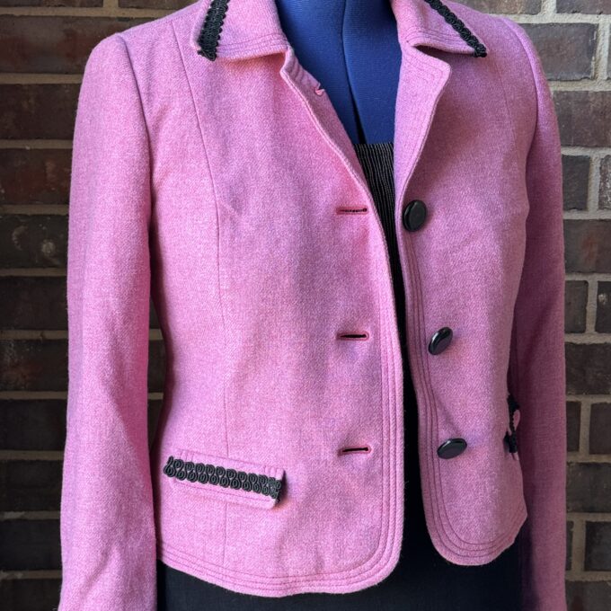 A pink jacket on a mannequin in front of a brick wall.