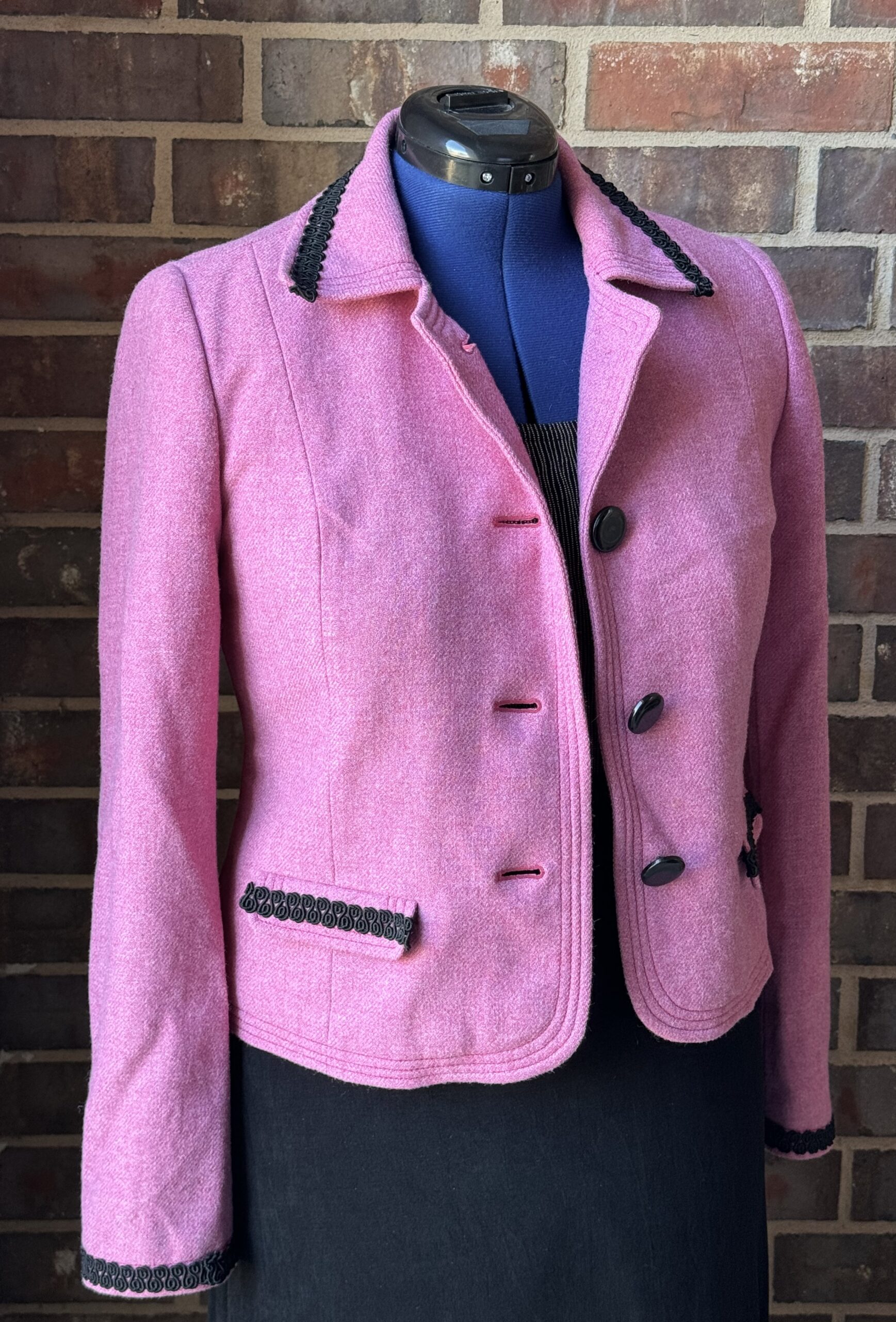A pink jacket on a mannequin in front of a brick wall.