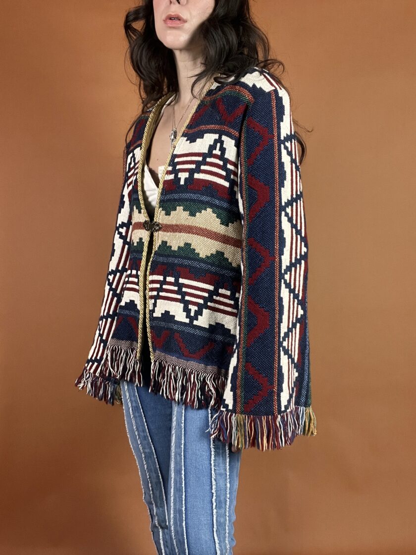 A woman wearing a sweater with fringes and jeans.