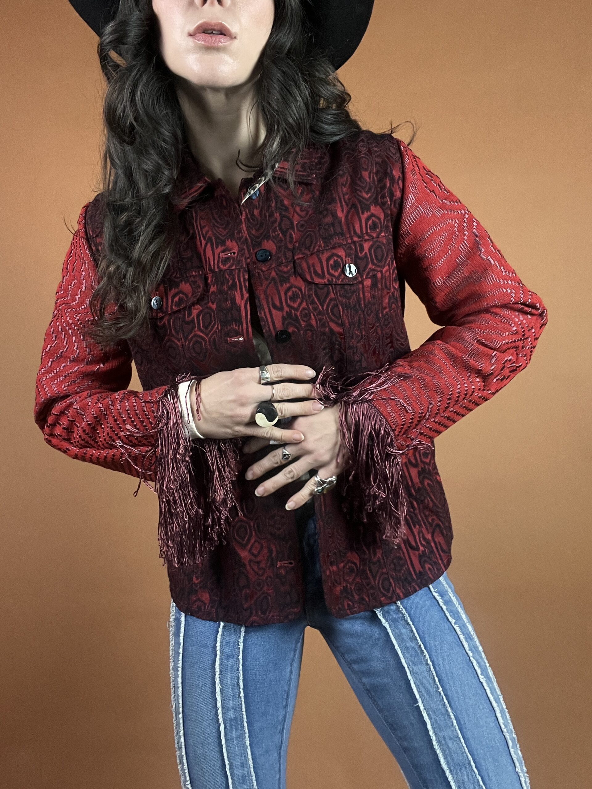 A woman in a hat and jeans wearing a red and black paisley jacket.