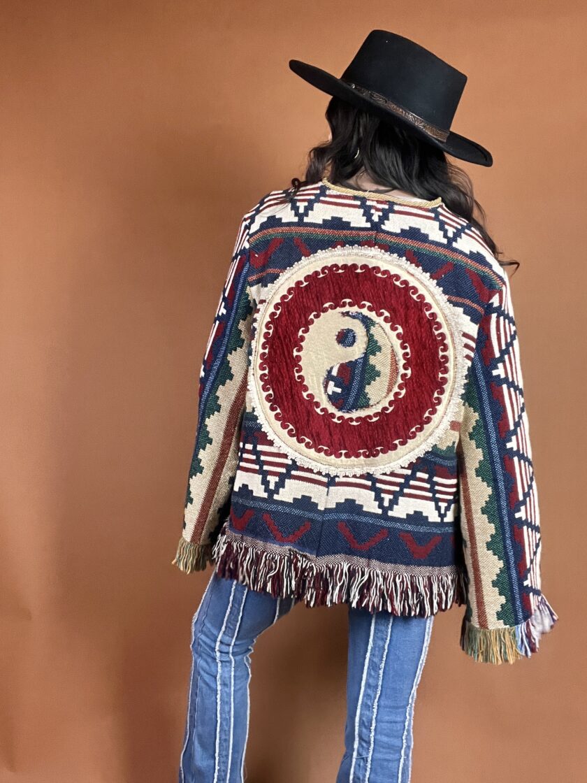 The back of a woman wearing a fringed jacket and jeans.