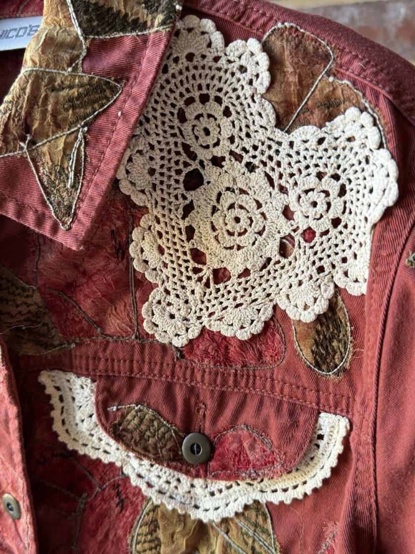 A close up of an upcycled red jacket with a white doily on it.