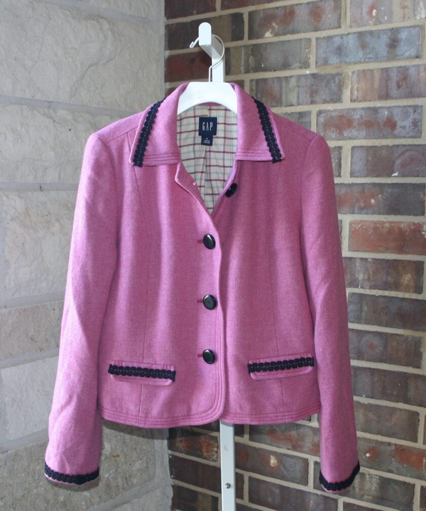 A pink jacket hanging on a mannequin in front of a brick wall.