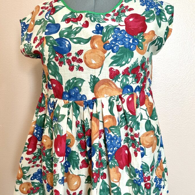 A girl's dress with fruit and berries on it.