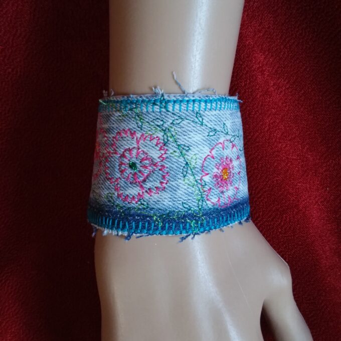 A denim cuff bracelet with embroidered flowers on it.
