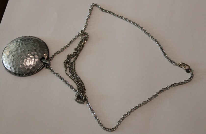 A silver hammered pendant on a chain.