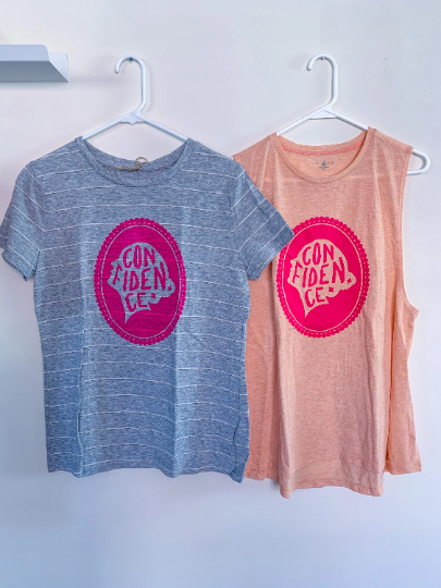 Two women's t - shirts hanging on a wall.