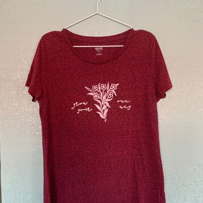 A women's red t - shirt hanging on a wall.