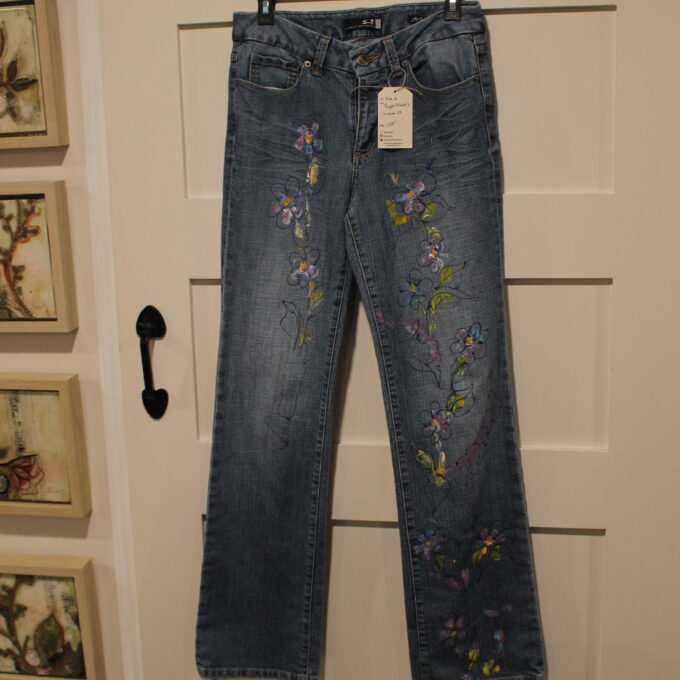 A pair of jeans with embroidered flowers hanging on a door.