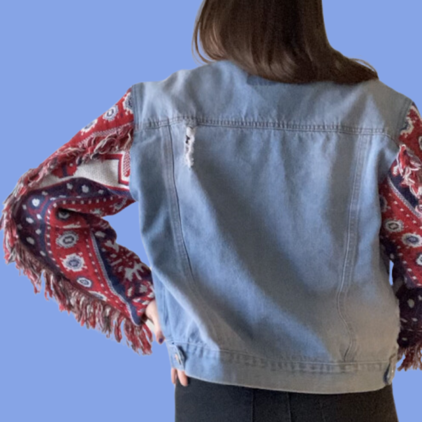 The back view of a woman wearing a denim jacket with fringes.