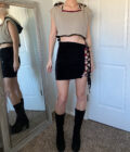 A woman standing in front of a mirror wearing black boots and a crop top.