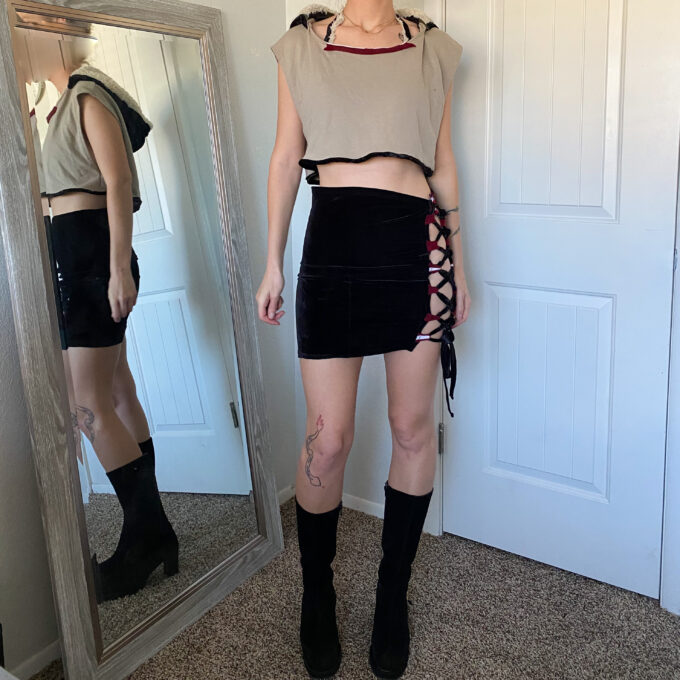 A woman standing in front of a mirror wearing black boots and a crop top.