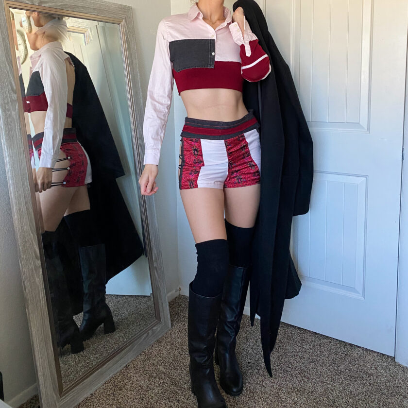 A woman is standing in front of a mirror wearing thigh high boots and a crop top.
